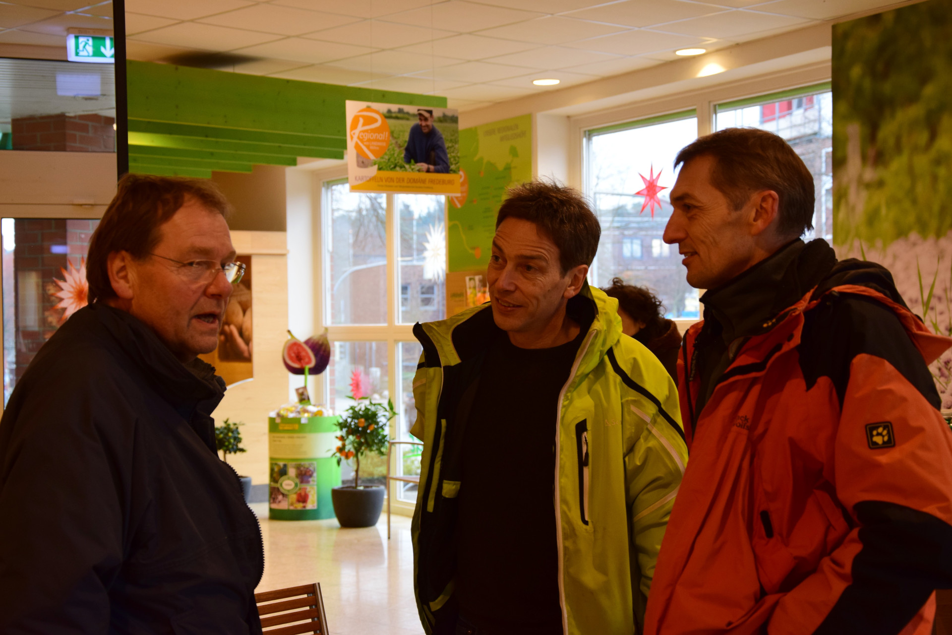 Drei Männer in einem Laden diskutieren angeregt miteinander.